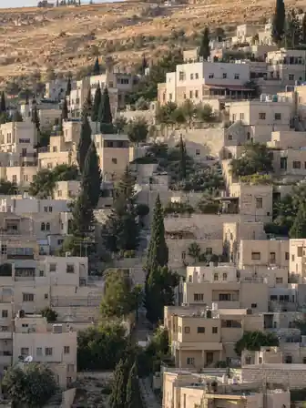 بيوت حجرية متدرّجة على منحدر جبلي شديد، مع جدران استنادية حجرية وأشجار سرو